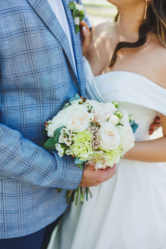 A bride and groom embracing with a bouquet of flowers between them.