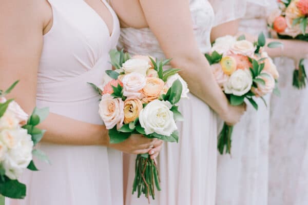 AdobeStock_1297159592_smol A group of bridesmaids in light pink dresses lined up and holding bouquets.