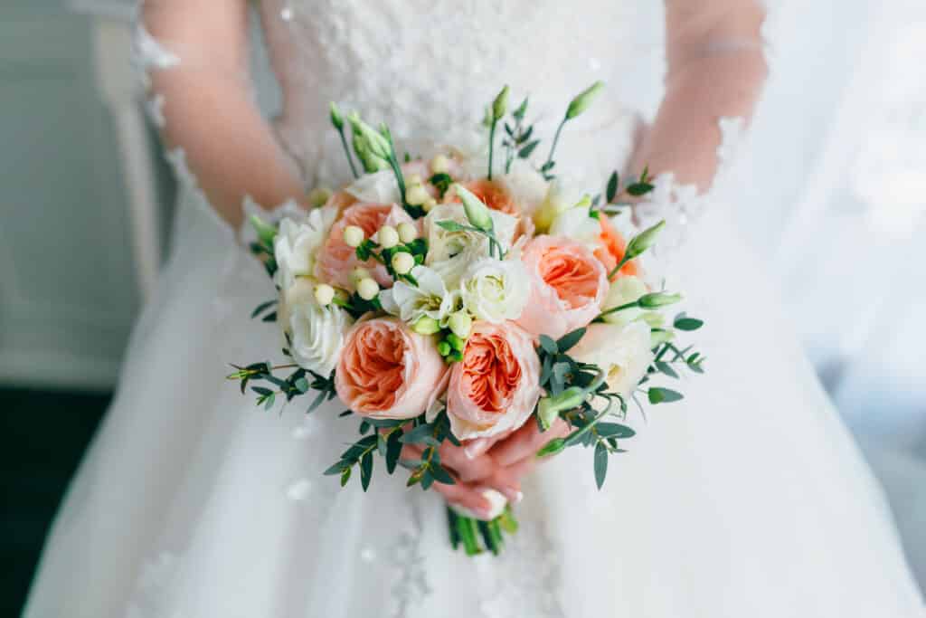 A bride in a white dress holding a pink, yellow and white bouquet of flowers.