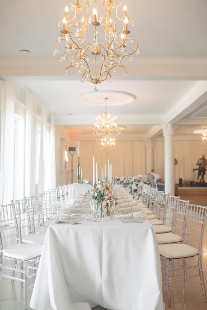 Elegantly set dining table in a bright, spacious event venue with chandeliers and floral arrangements
