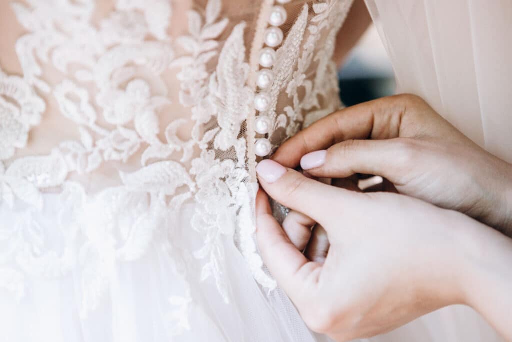 A bridesmaid helping a bride fasten the back of her dress.