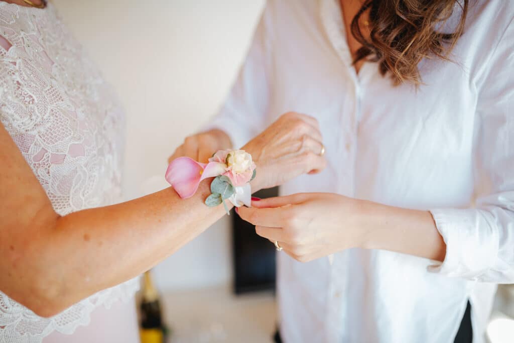 A woman helping a bride tie a corsage to her wrist.