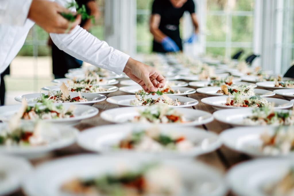 A table filled with plates of food being prepped and garnished by event staff.