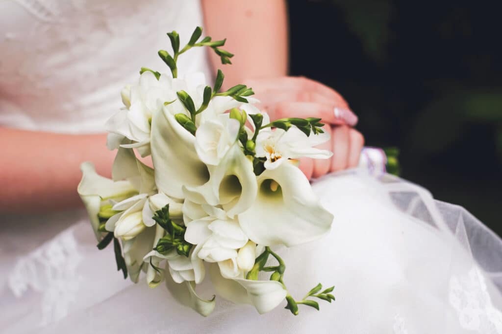 A bride in a white wedding dress holds a wedding bouquet of white calla lilies