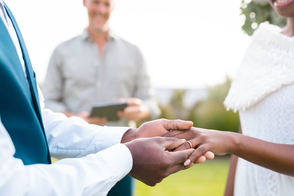 Groom slipping a wedding ring on his bride's finger during outdoor ceremony.