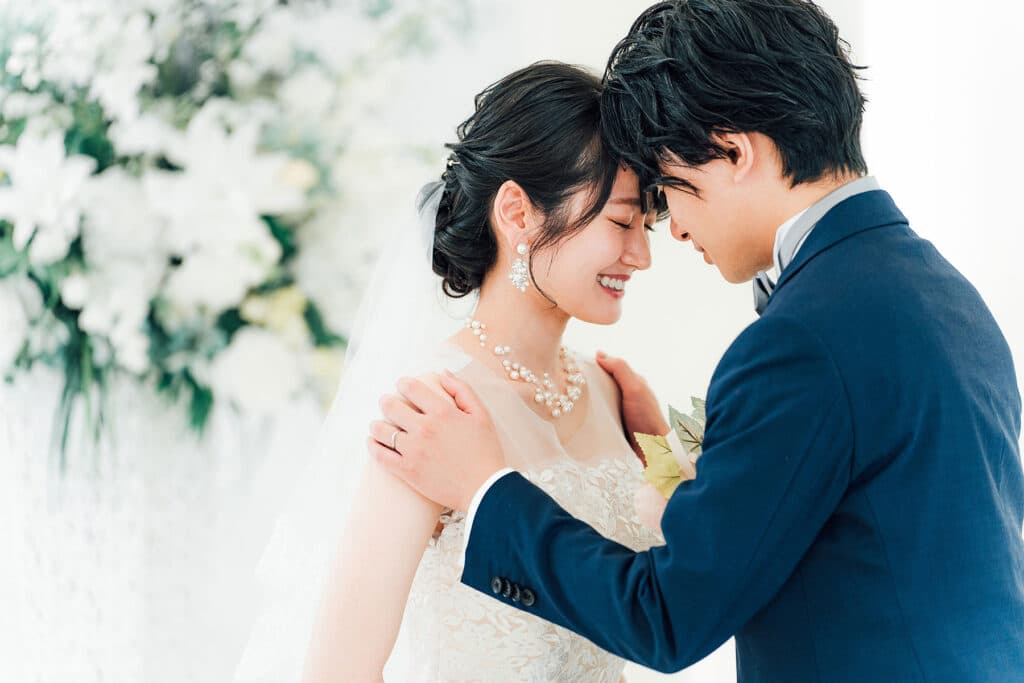 A bride and groom touching foreheads with their eyes closed in full wedding regalia.
