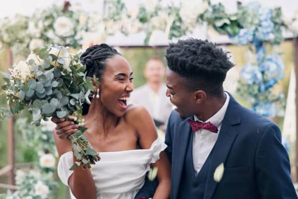 AdobeStock_652477649_web Bride and groom looking at each other and giving excited open-mouthed smiles at each other as they walk back up the aisle at the end of the wedding ceremony.