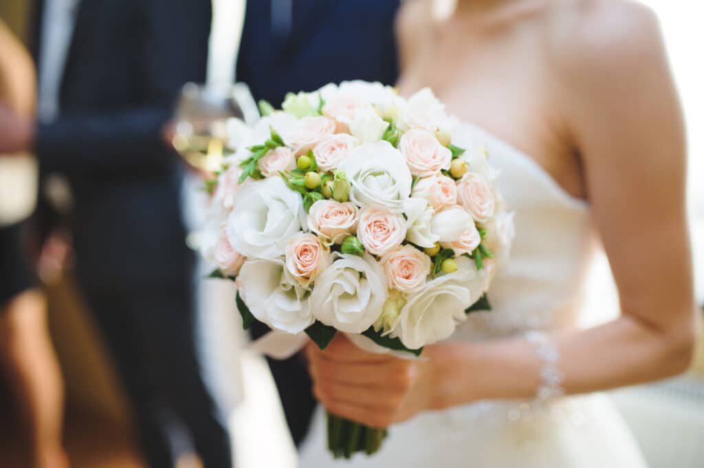 A bride in white clutching a bouquet of white, pink and yellow flowers.