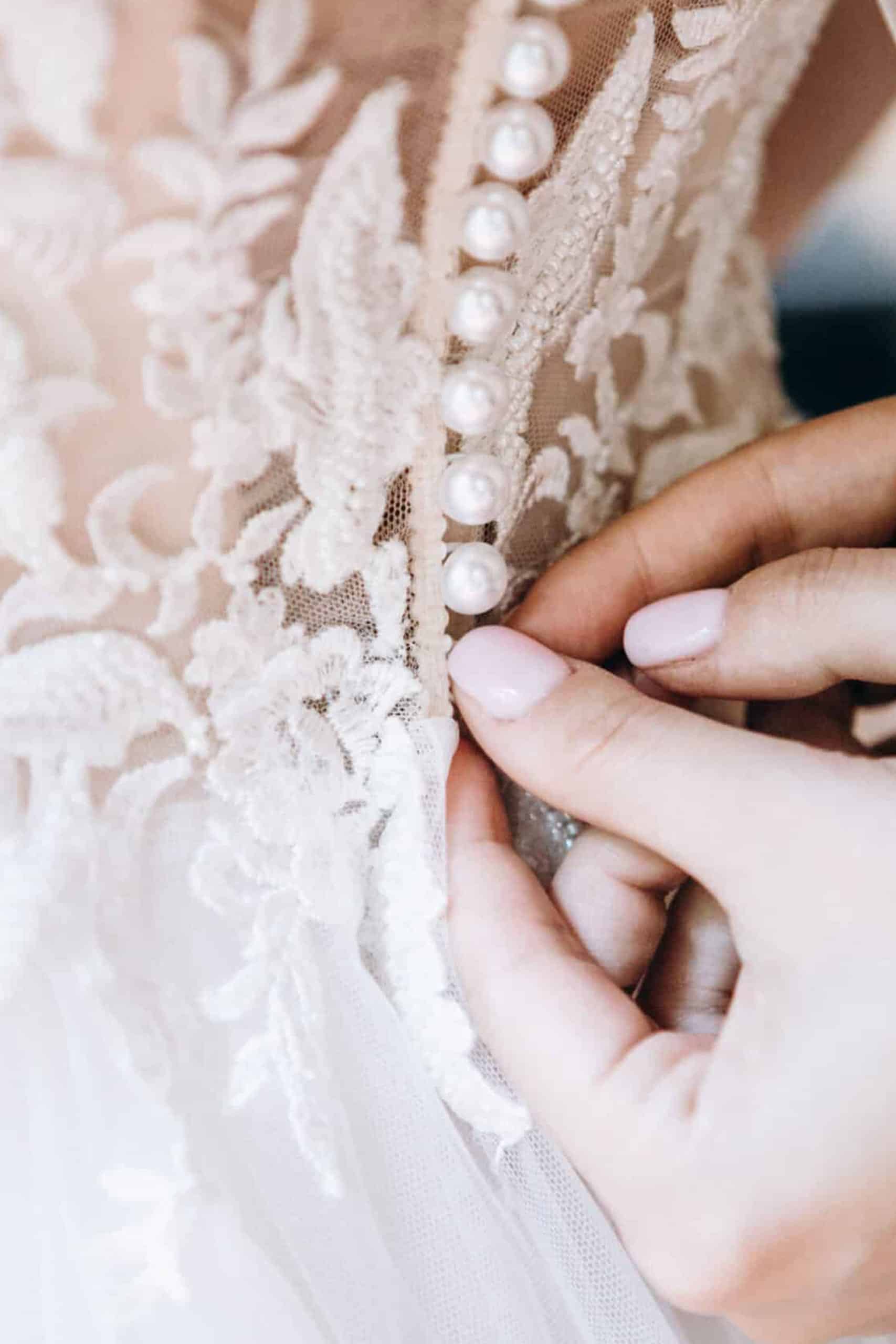 A bridesmaid helping a bride fasten the back of her dress.