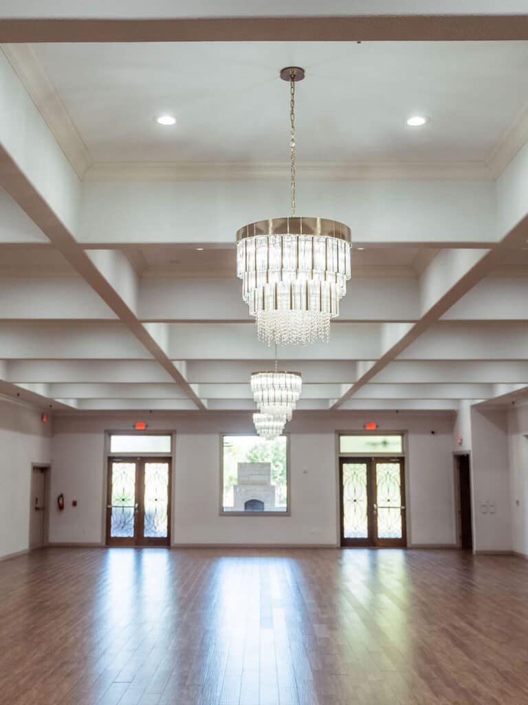 Empty event venue with wood floors, chandeliers, and exposed ceiling beams.